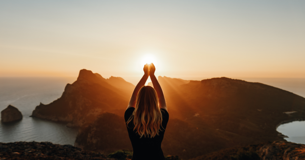 夕日を背に両手を上げる人物の後ろ姿。恋の願いを占いで整え前向きになるイメージ